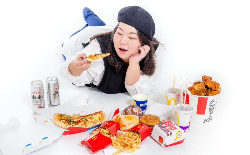 休みの日は頬杖をついてジャンクフードを食す女性の写真