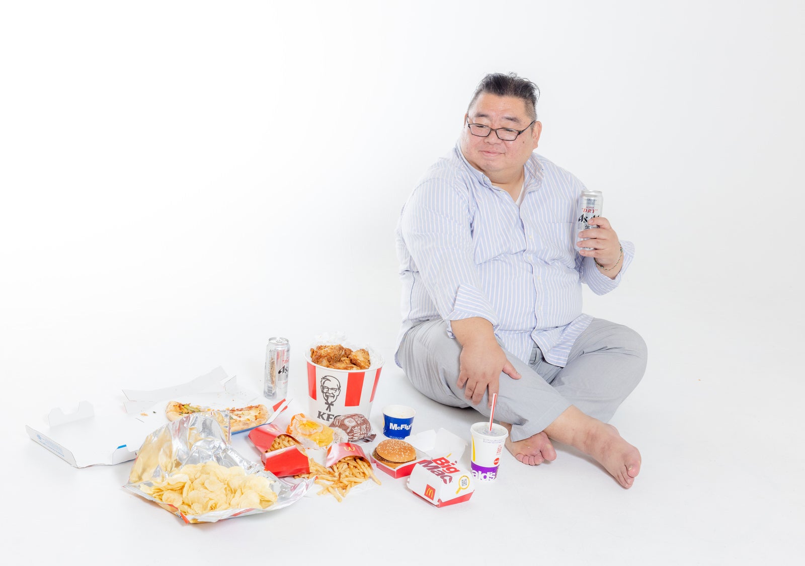 「揚げ物やハンバーガーなどに囲まれてほっこりする肥満男性」の写真［モデル：ダルマ親方］