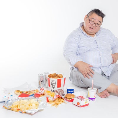 ジャンクフードを食べ過ぎてお腹を押さえる男性の写真
