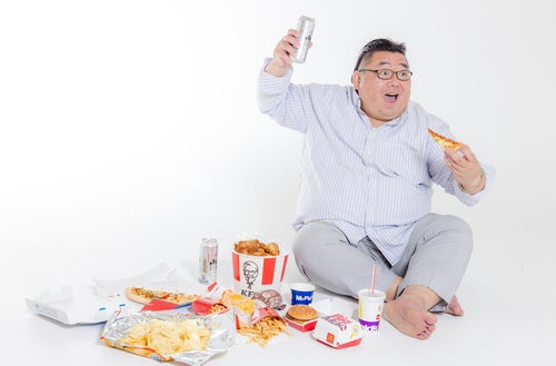 ジャンクフードを食べながら観戦する肥満の写真