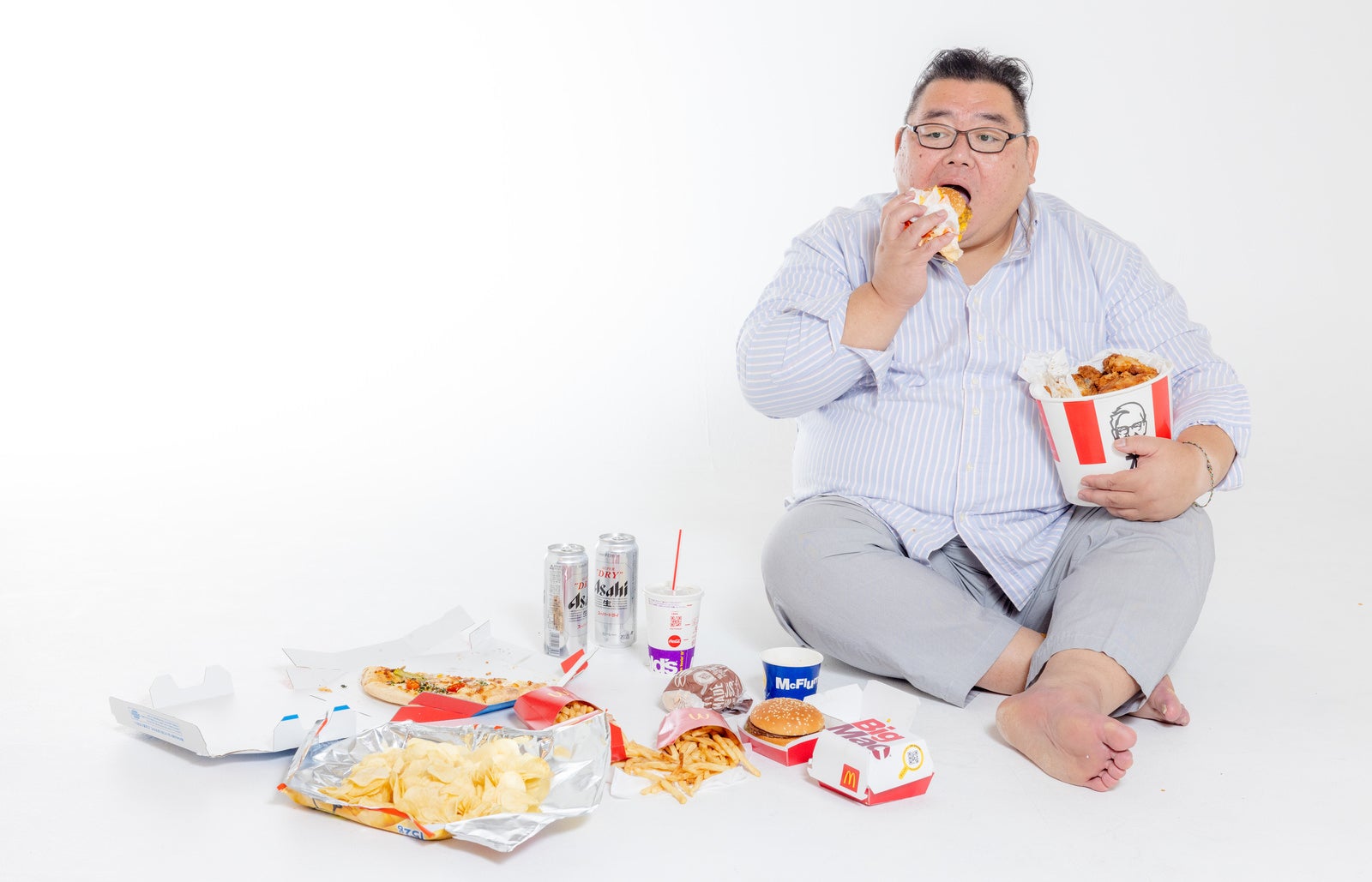「ハンバーガーを食すジャンクフードに囲まれた男性」の写真［モデル：ダルマ親方］
