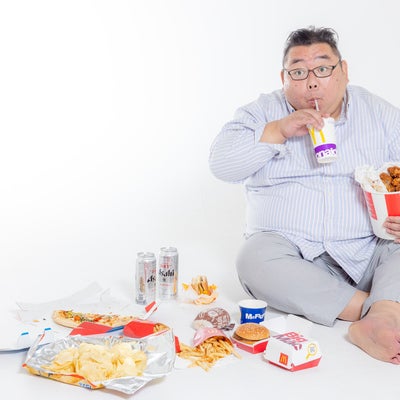 座り込んでファーストフードを暴飲暴食するストレス男性の写真