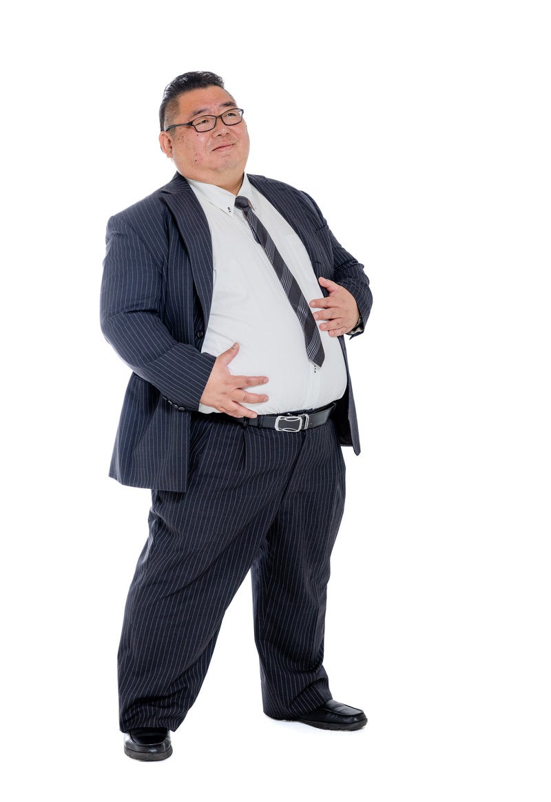 「お腹周りに付いた贅肉を気にするスーツ姿の男性」の写真［モデル：ダルマ親方］