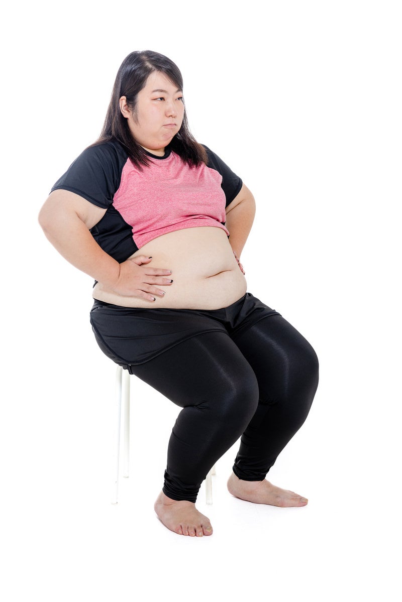 「椅子に腰掛けてダイエットに励む膨よかな女性」の写真［モデル：KANA］