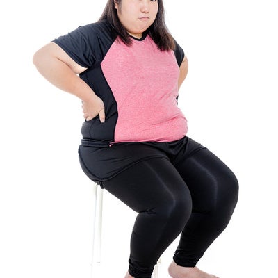 腰に手を当て椅子に座るダイエット中の膨よかな女性の写真