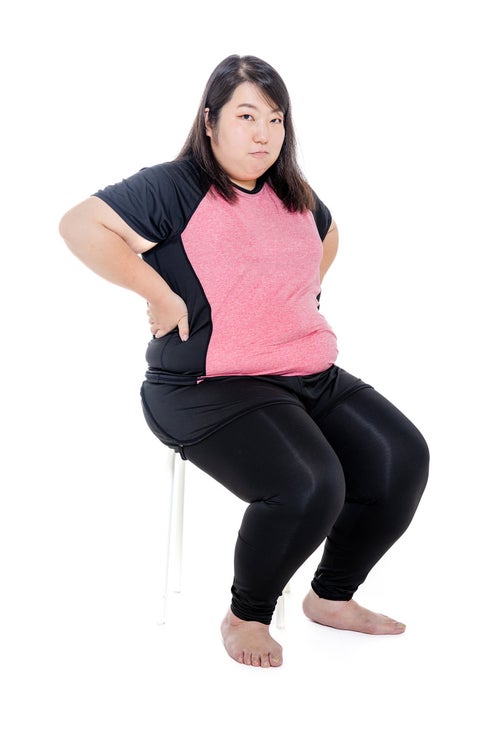 腰に手を当て椅子に座るダイエット中の膨よかな女性の写真