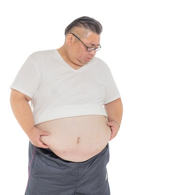 お腹に付いた贅肉をかかえる男性の写真