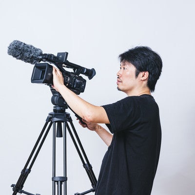 ビデオカメラ用の三脚に取り付けて撮影する現場のカメラマンの写真