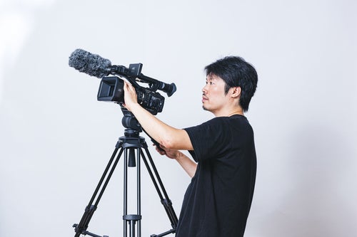 ビデオカメラ用の三脚に取り付けて撮影する現場のカメラマンの写真