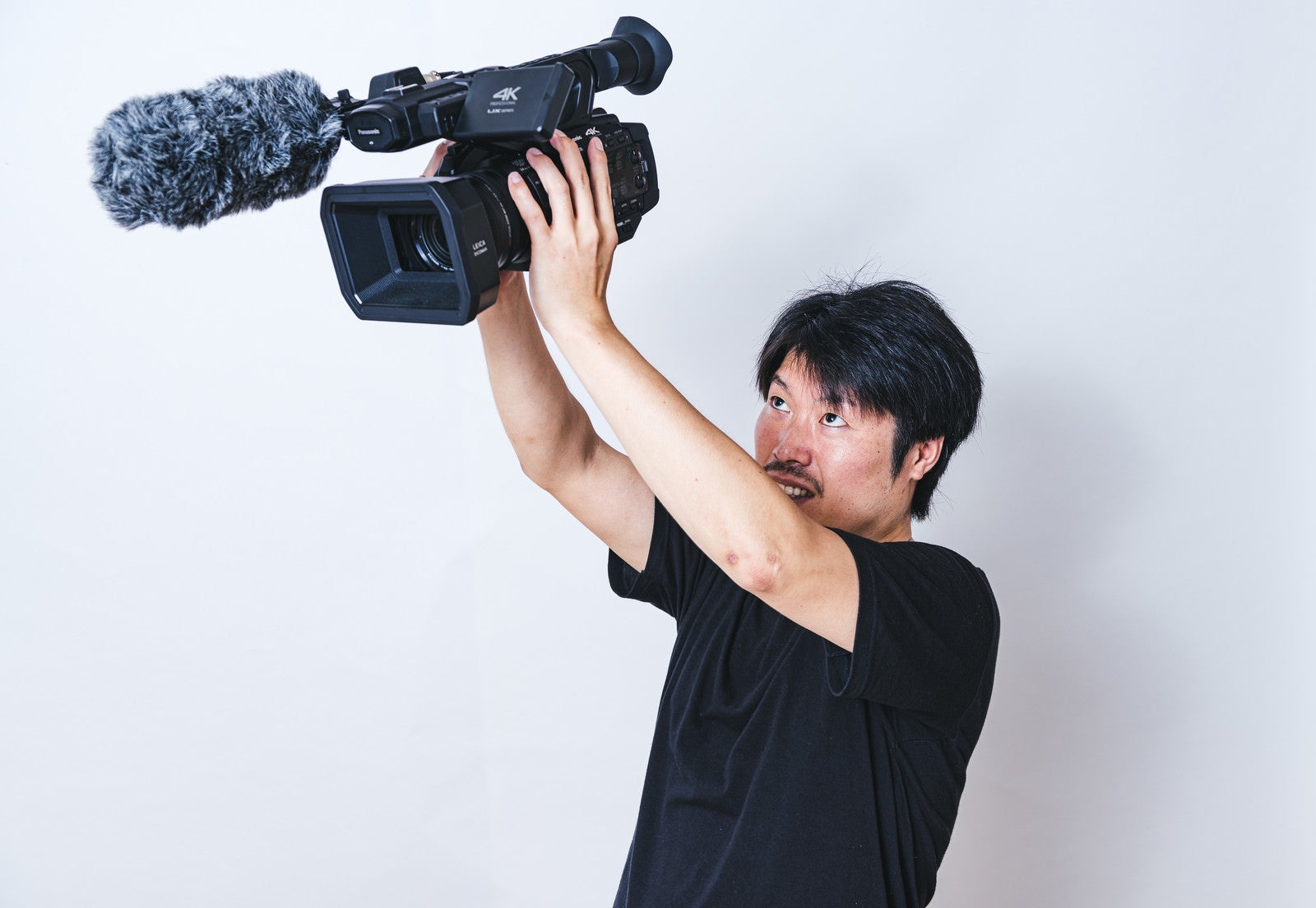 「両手を伸ばして高い位置からムービー撮影するカメラマン」の写真［モデル：瀧野恵太］