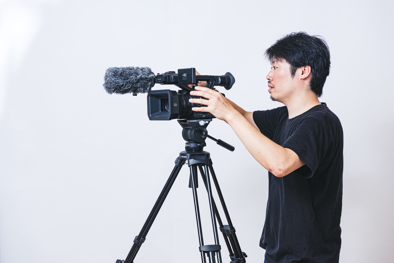 「三脚に業務用4Kビデオカメラを取り付けるカメラマン」の写真［モデル：瀧野恵太］