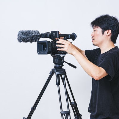 三脚に業務用4Kビデオカメラを取り付けるカメラマンの写真