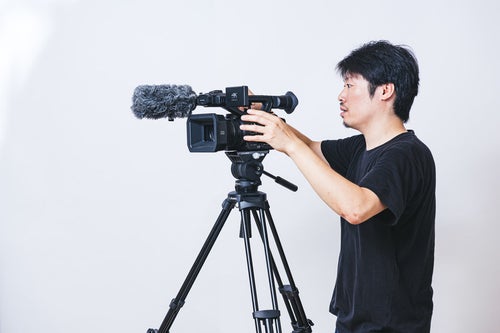 三脚に業務用4Kビデオカメラを取り付けるカメラマンの写真