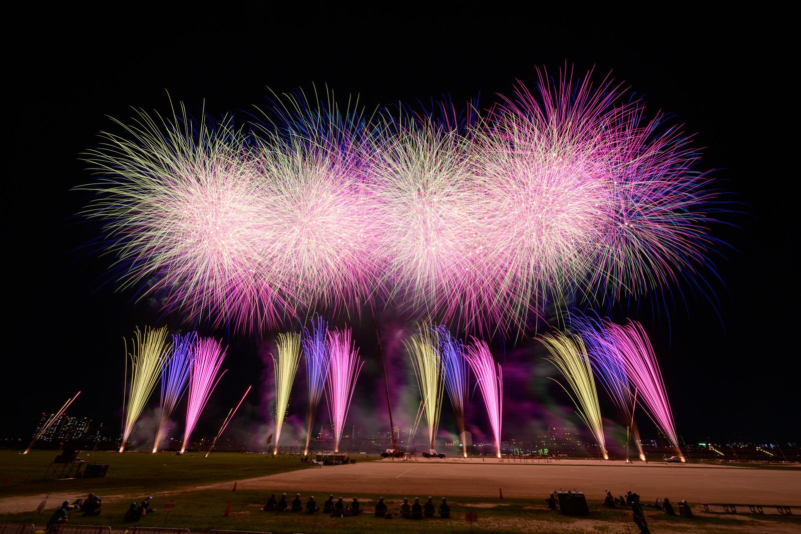 「江戸川の河川敷で打ち上げられる花火の様子」の写真