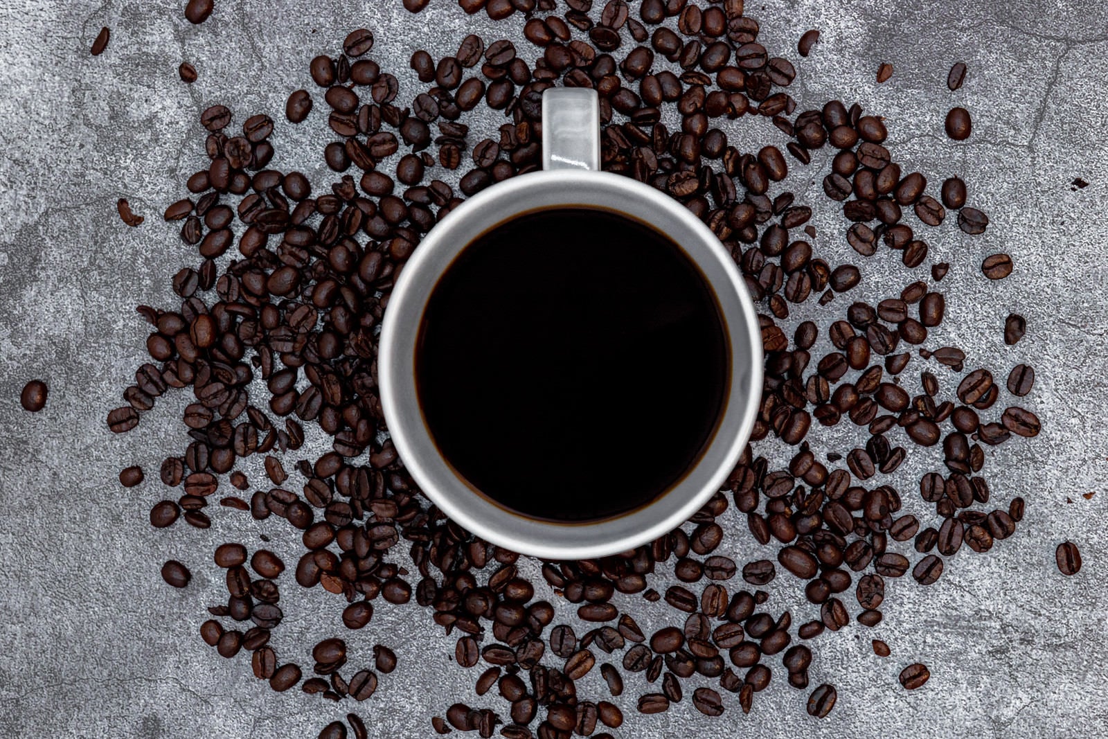 「コーヒーカップの周りを囲うコーヒー豆」の写真