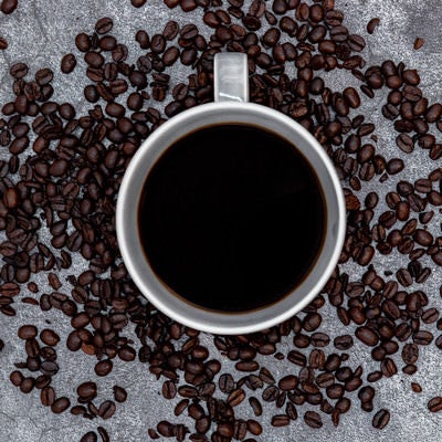 コーヒーカップの周りを囲うコーヒー豆の写真