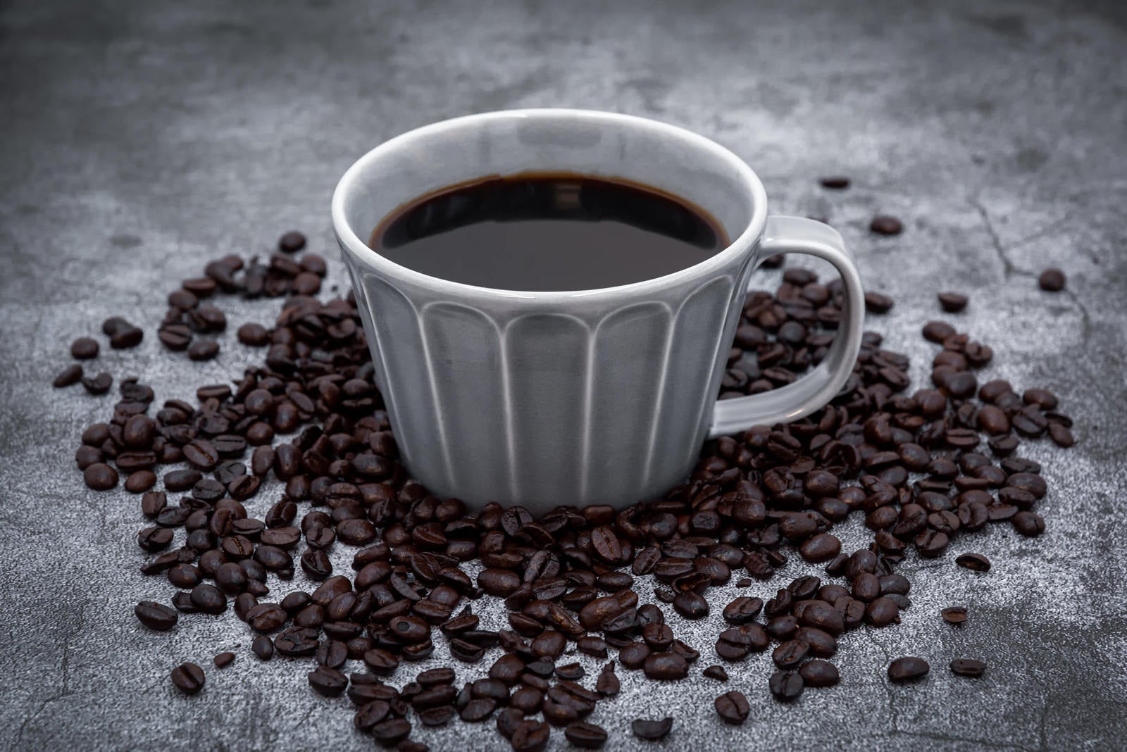 「コーヒーカップ周りのコーヒー豆」の写真