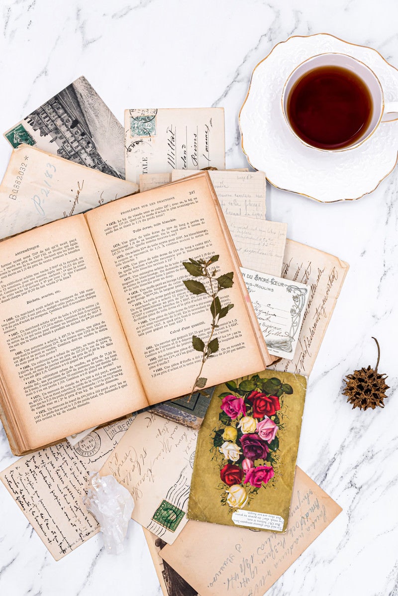 「散らばった手紙と古書に添えられたコーヒーカップ」の写真