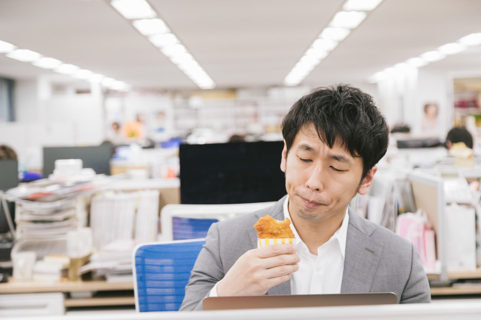 「仕事中に骨なしフライドチキンを食べるサラリーマン」の写真［モデル：大川竜弥］
