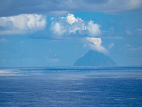 霞むパステル色の海と空の中に三角形の姿を見せる南硫黄島の写真
