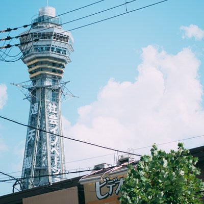 白い雲と青空をバックにした通天閣と緑豊かな新世界の日常風景の写真