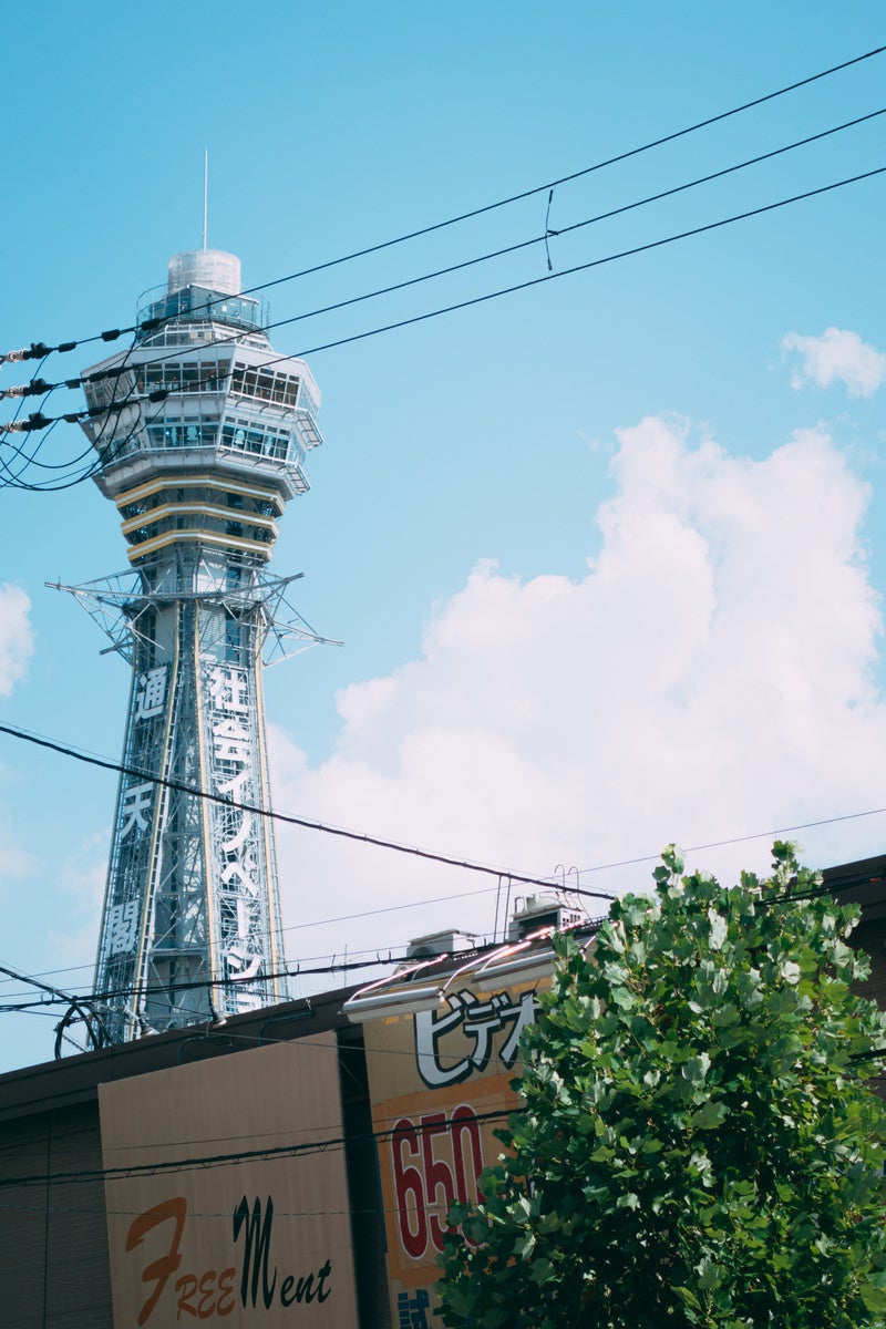 白い雲と青空をバックにした通天閣と緑豊かな新世界の日常風景の写真