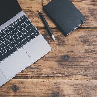 MacBookと手帳とペンで作業する机上の写真