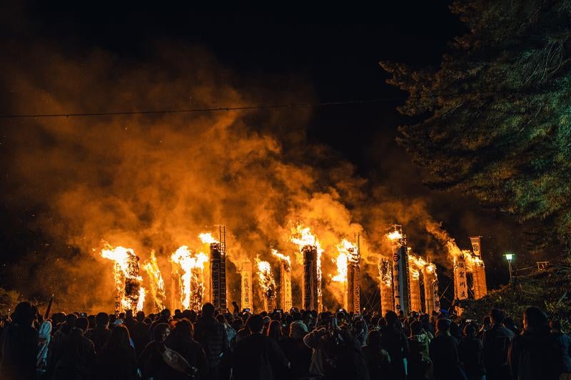 大松明から立ち上る煙を染める火祭りの炎の写真