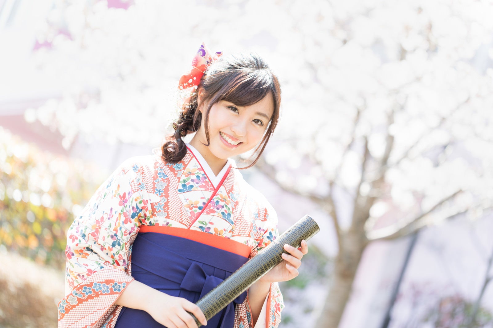 「桜の花と卒業証書を持った袴姿の女性」の写真［モデル：河村友歌］