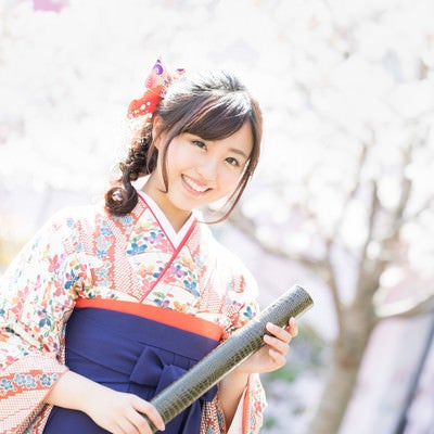 桜の花と卒業証書を持った袴姿の女性の写真