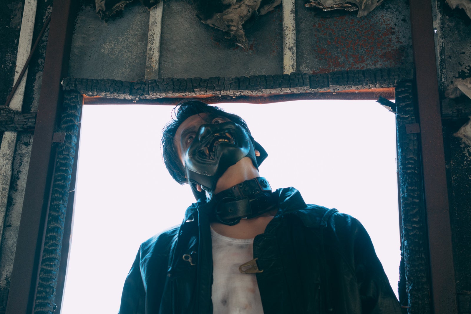 黒いライダースジャケットとサングラスの男性が廃墟の窓から上を見上げている［モデル：花和瞭］