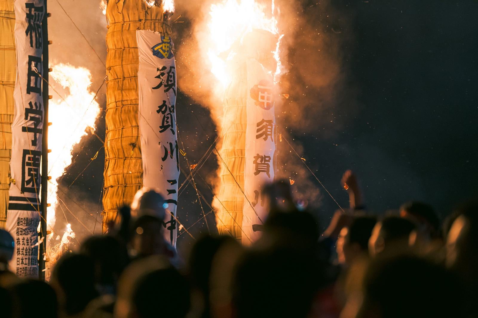 「大松明の炎と飛び散る火花を見守る観客」の写真