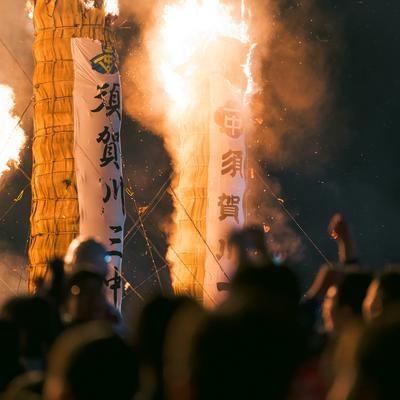大松明の炎と飛び散る火花を見守る観客の写真