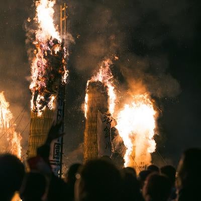 燃え上がる火柱に見入る松明あかしの見物客の写真