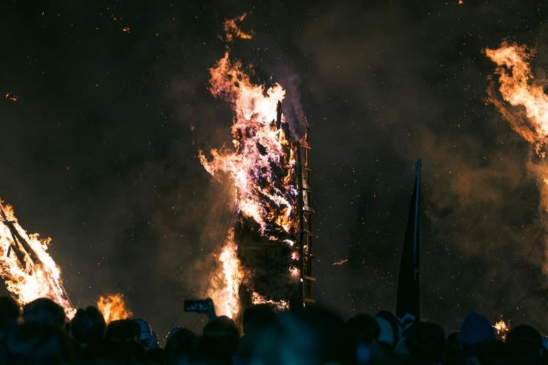 風に舞う火花と立ち上がる炎に歓喜する観客の写真