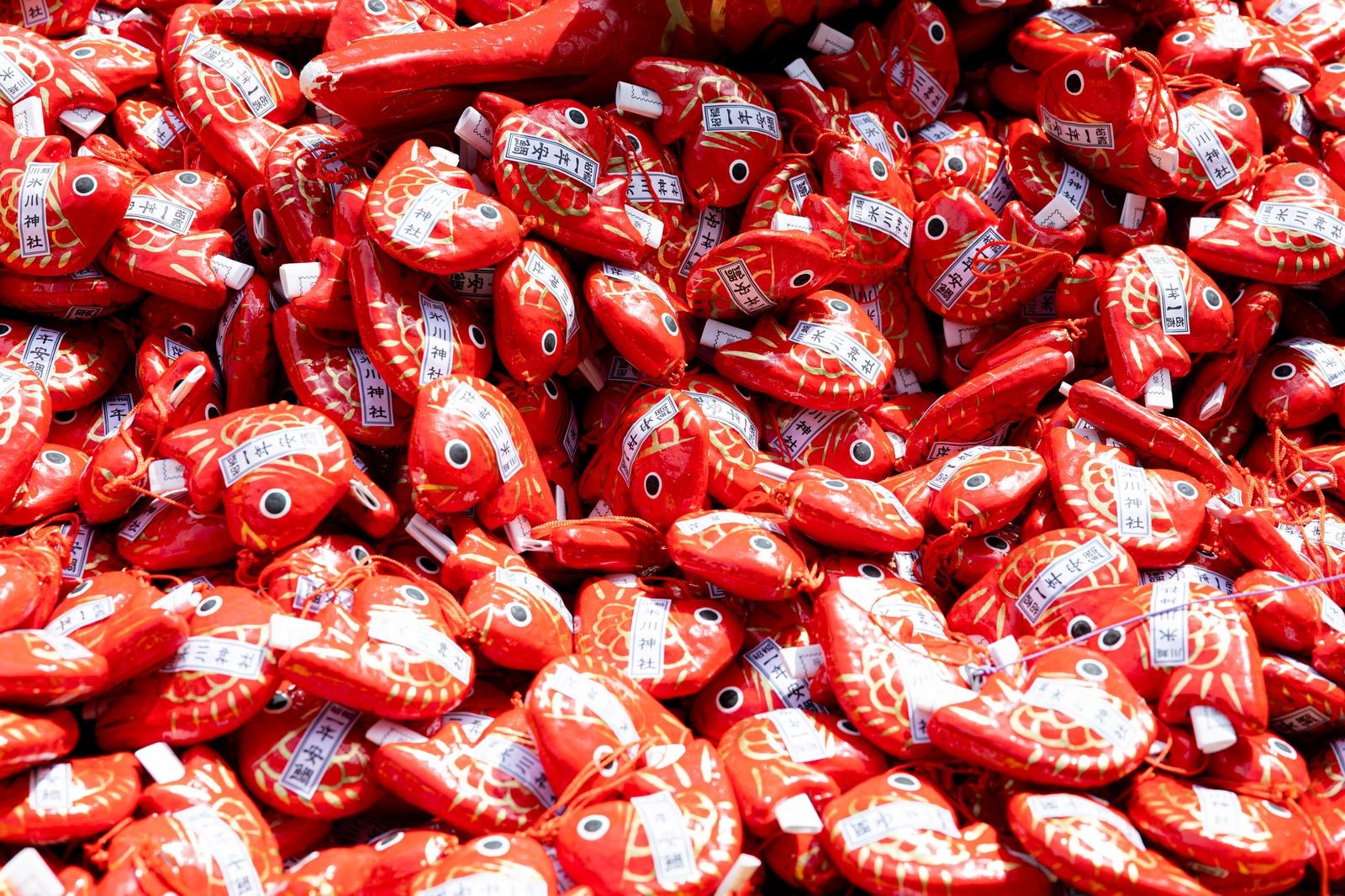 Red fabric fish-shaped fortune slips (tai omikuji) stacked together, each with white labels and strings attached