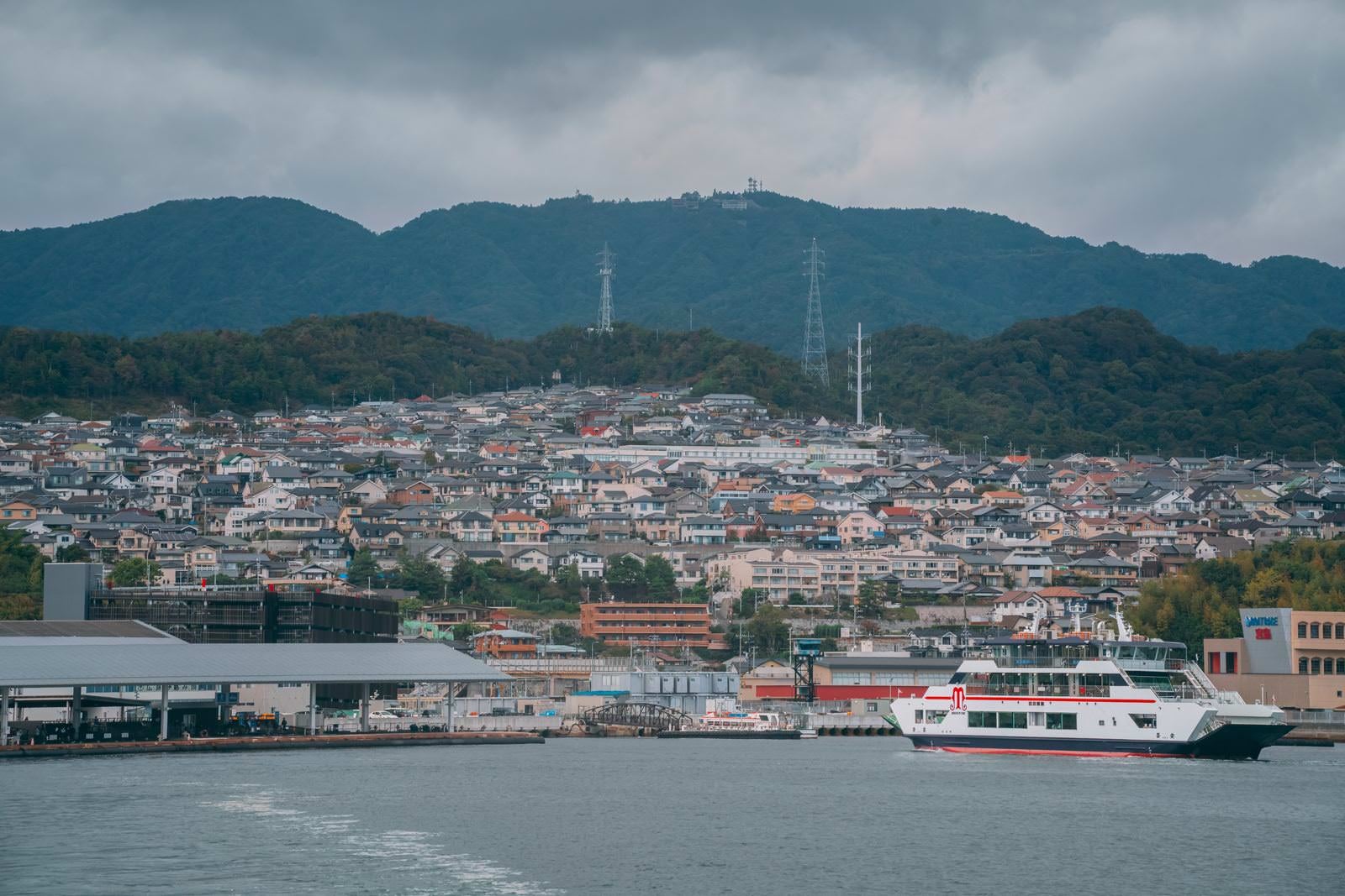 青い海を航行する白いフェリーみせん丸と背景の住宅地