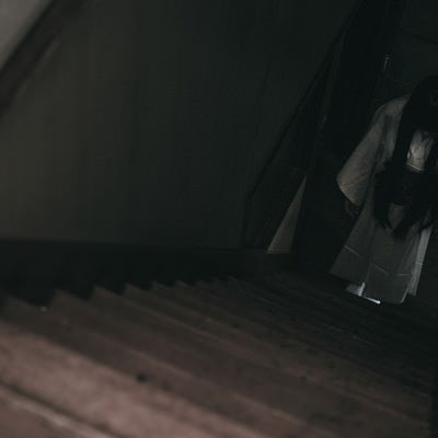 暗い階段下に白装束の女性がうつむき竚むの写真