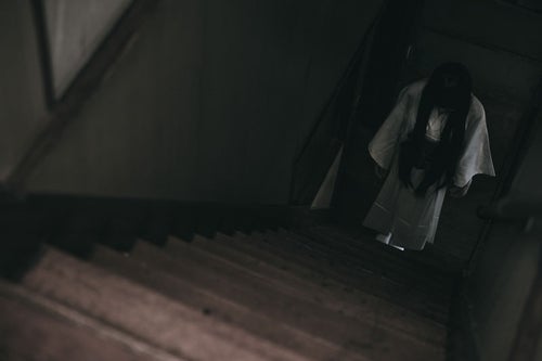 暗い階段下に白装束の女性がうつむき竚むの写真