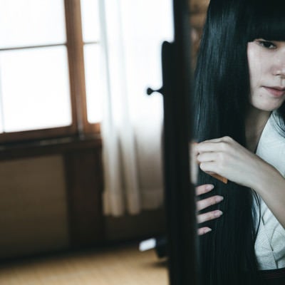 黒髪の日本人女性が櫛で髪をとく様子の写真
