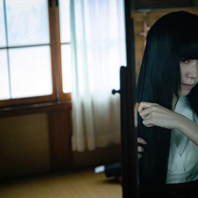 鏡を見ながら長い黒髪をとかす女性の写真