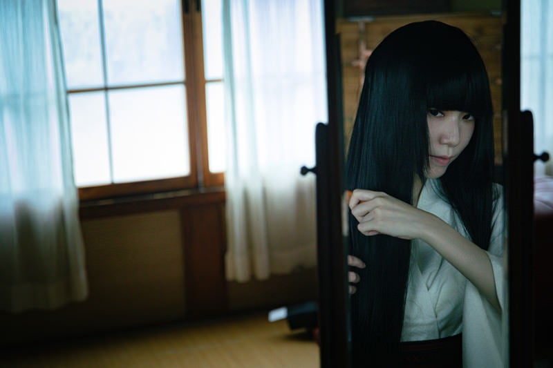 鏡を見ながら長い黒髪をとかす女性の写真