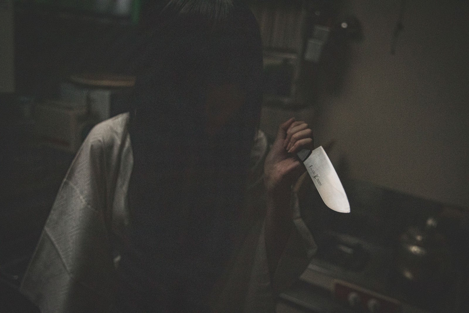 「暗がりで包丁を持つ黒髪の女性」の写真［モデル：緋真煉］