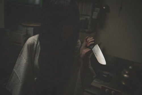 暗がりで包丁を持つ黒髪の女性の写真