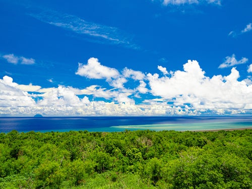 海底噴火によって変色した翁浜沖の海域と遠くに見える雲に頭を隠した南硫黄島の写真