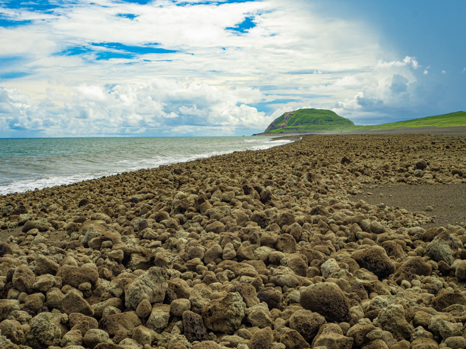 「翁浜に漂着した無数の岩塊と摺鉢山」の写真