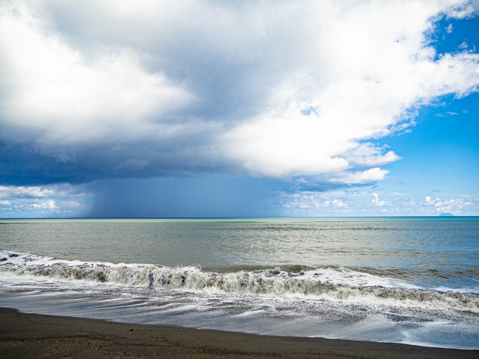 「翁浜から見る海面に降りるスコールの柱と南硫黄島」の写真