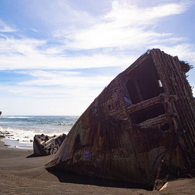 硫黄島千鳥ヶ浜の波打ち際に横たわる船の残骸と続く白波の写真
