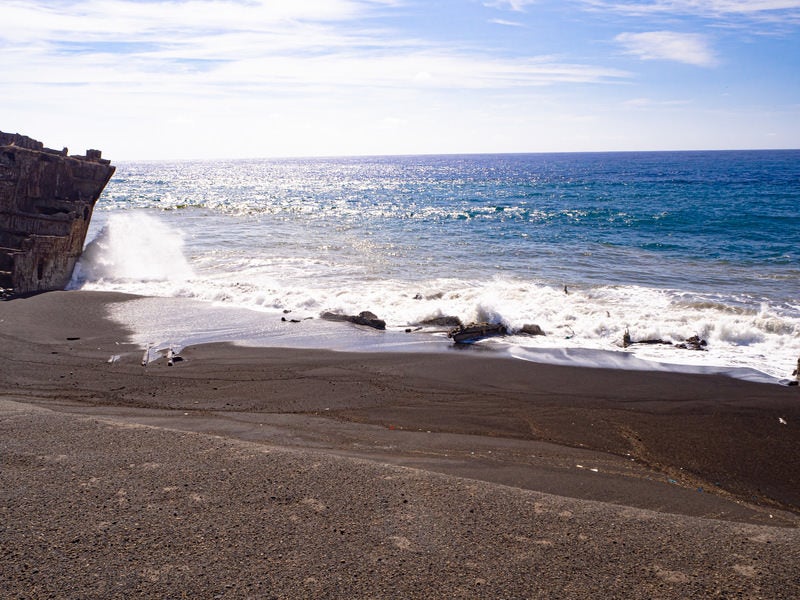 千鳥ヶ浜の波打ち際に散乱する瓦礫にぶつかり砕ける波の写真