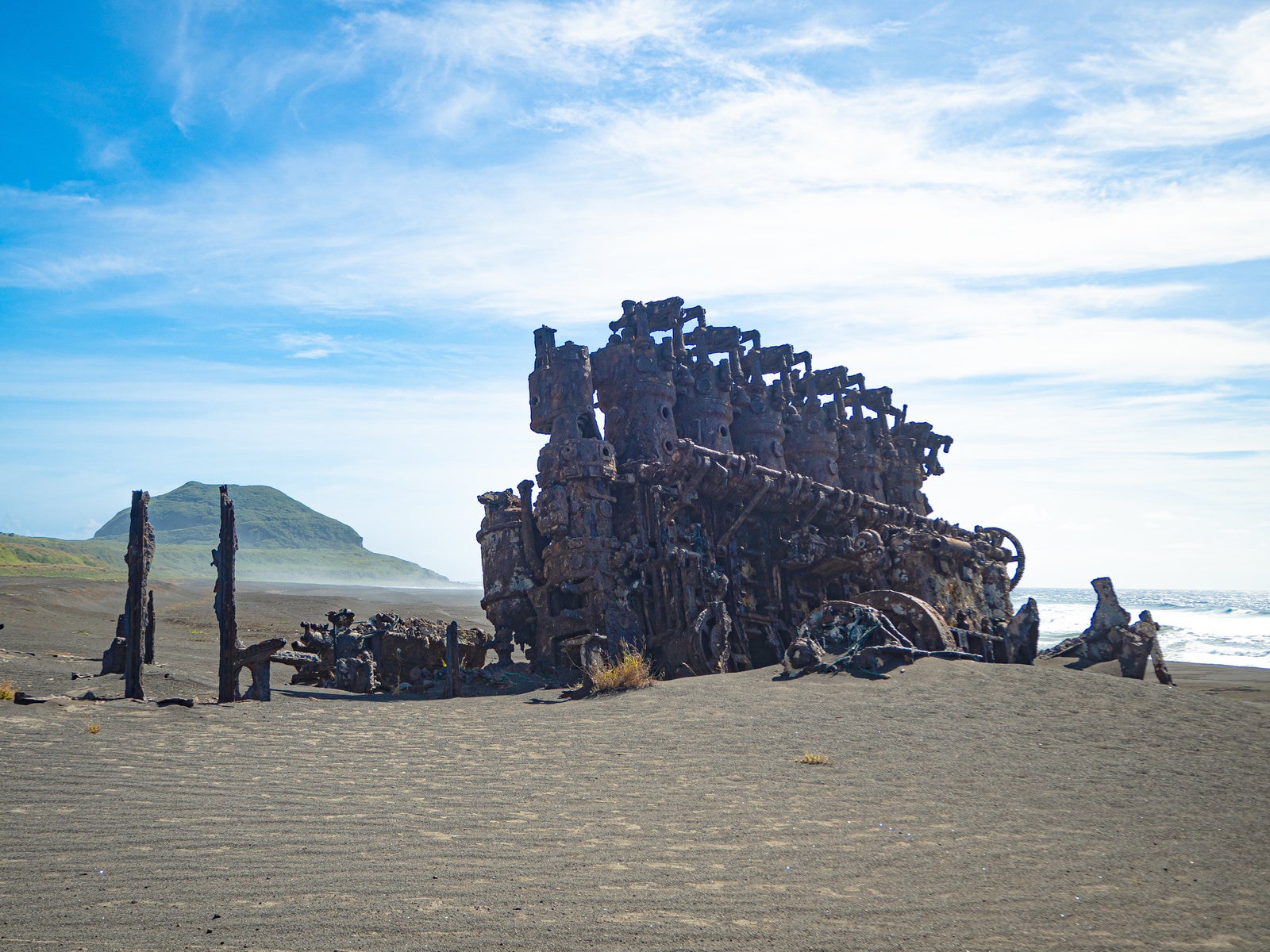 千鳥ヶ浜の沈船のエンジンなどの残骸と強い風で流れるしぶきに霞む砂浜の奥に立つ摺鉢山 photo